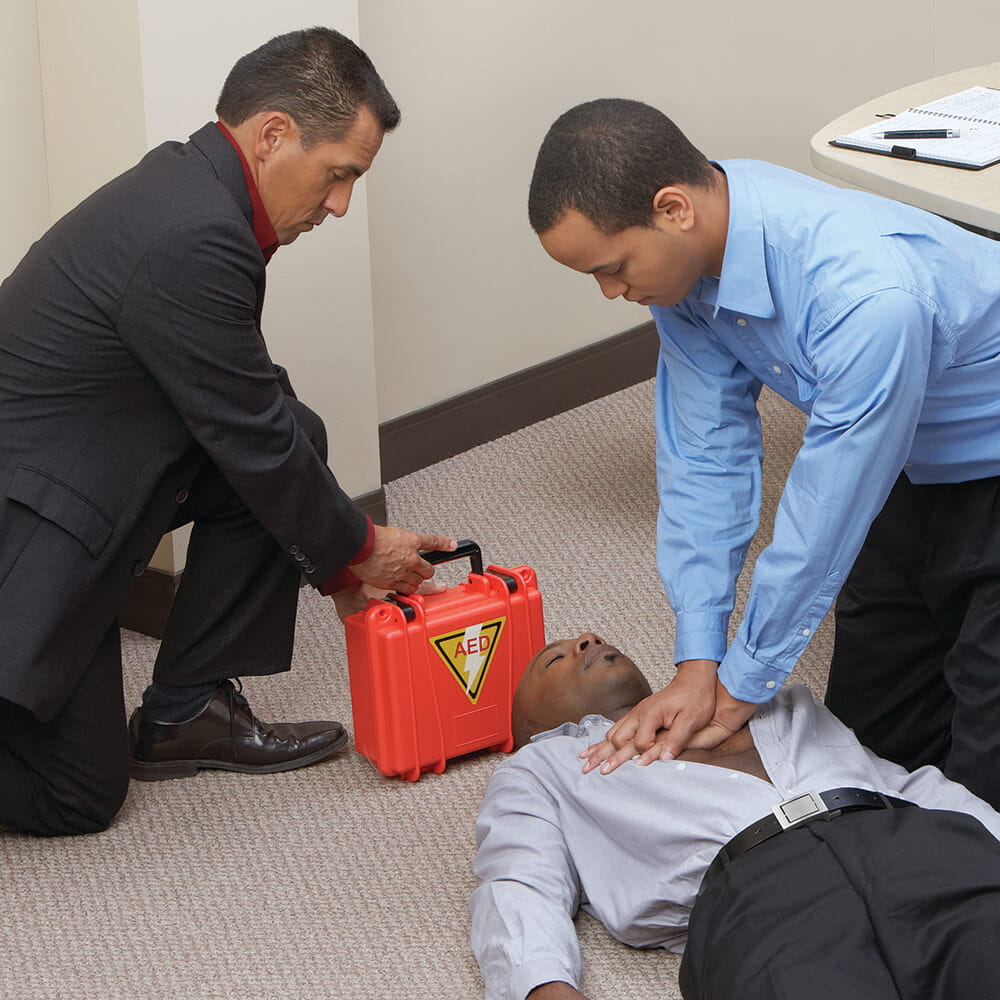 man performing CPR in workplace and another man holding an AED image
